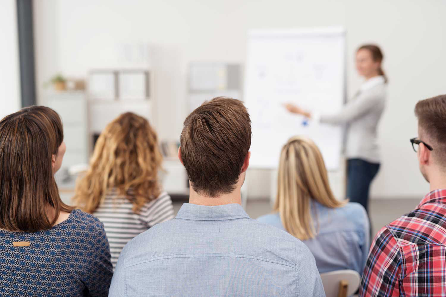 Firmenunterricht: Eine Gruppe Männer und Frauen folgt dem Unterricht. Der ur-welcome Sprachcoach erläutert am Whiteboard.