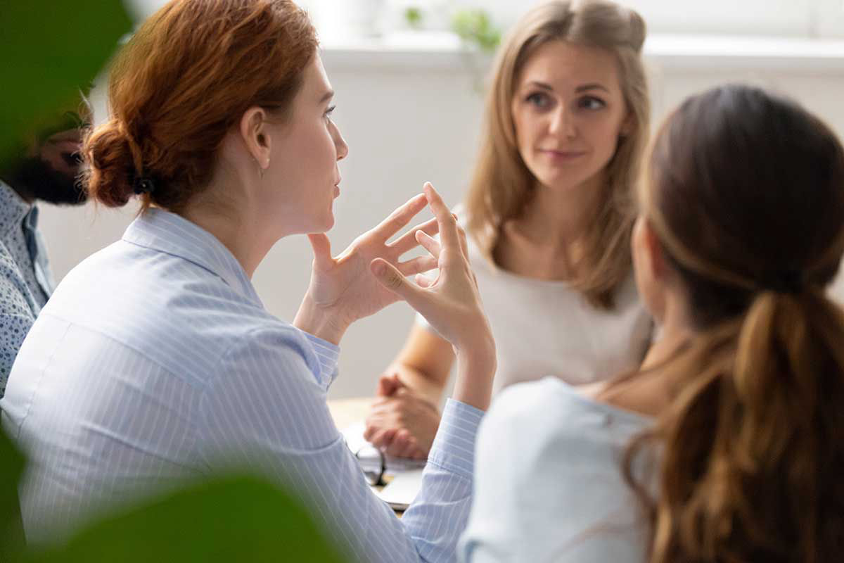 Sprachcoaching für Privatpersonen und Unternehmen. Eine Gruppe von drei Frauen und einem Mann sitzen diskutierend zusammen.